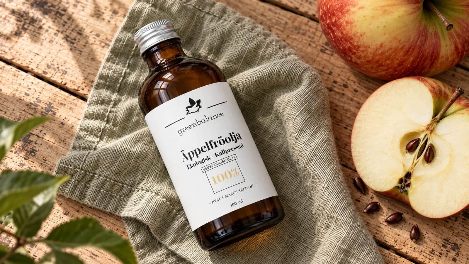 appelfroolja produkt ravaror Flaska med äppelfröolja liggande på linne och trä, med äpple och äppelkärnor.