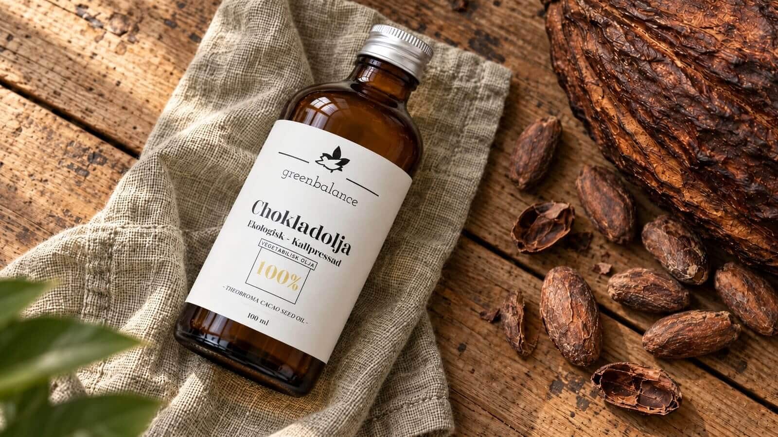 chokladolja produkt ravaror Flaska med chokladolja liggande på linne och trä, med kakaofrukt och kakaobönor.