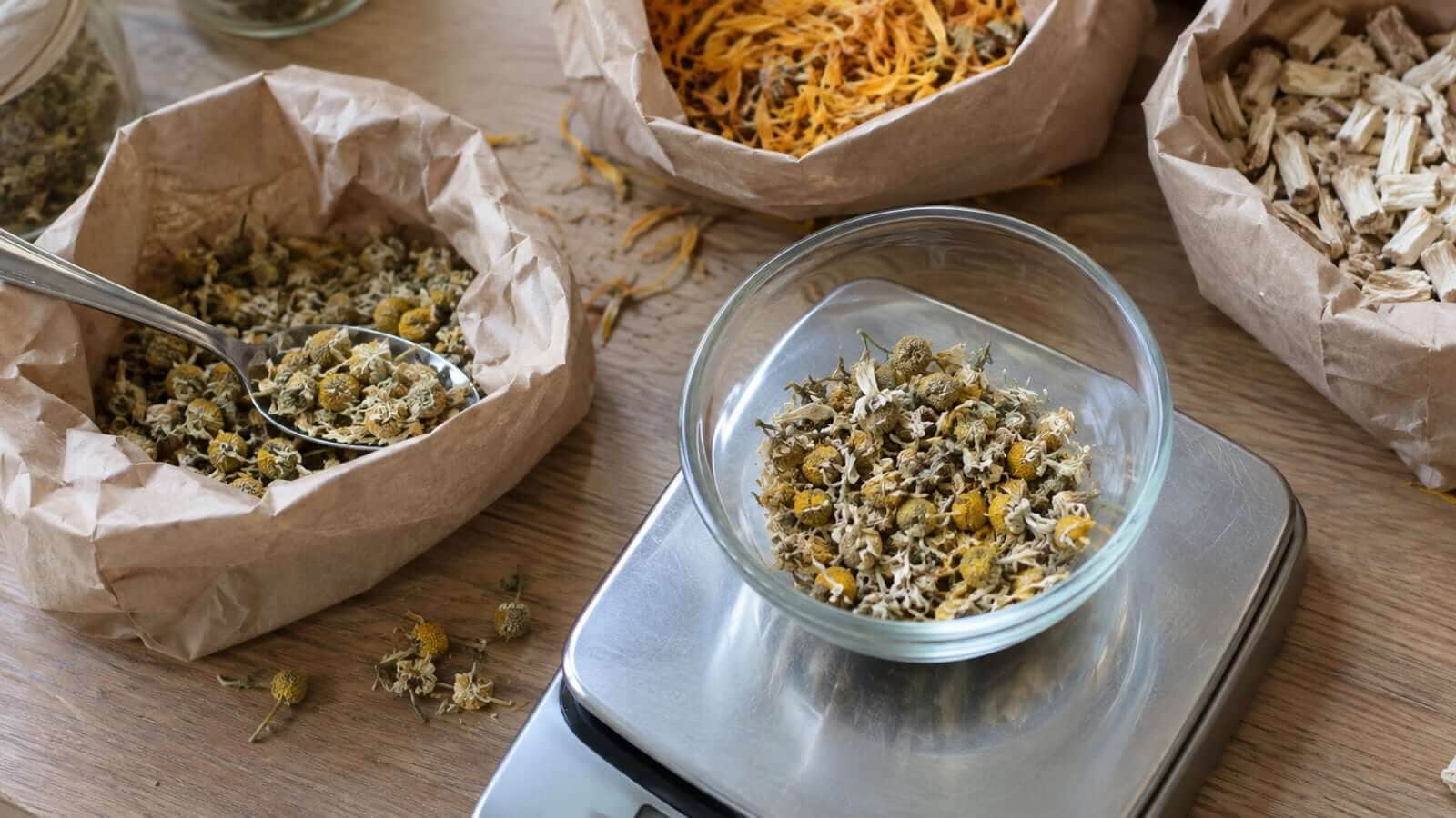glycerit orter uppvagning En liten mängd torkad kamomill vägs upp intill öppnade förpackningar med örtråvaror