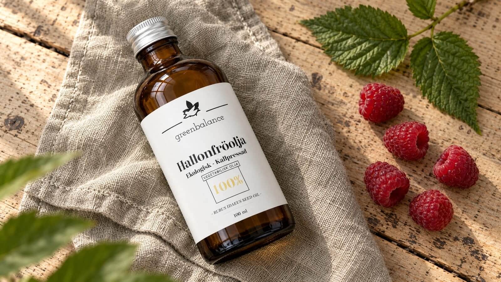 hallonfroolja produkt ravaror Flaska med hallonfröolja liggande på linne och trä, med hallon och blad.