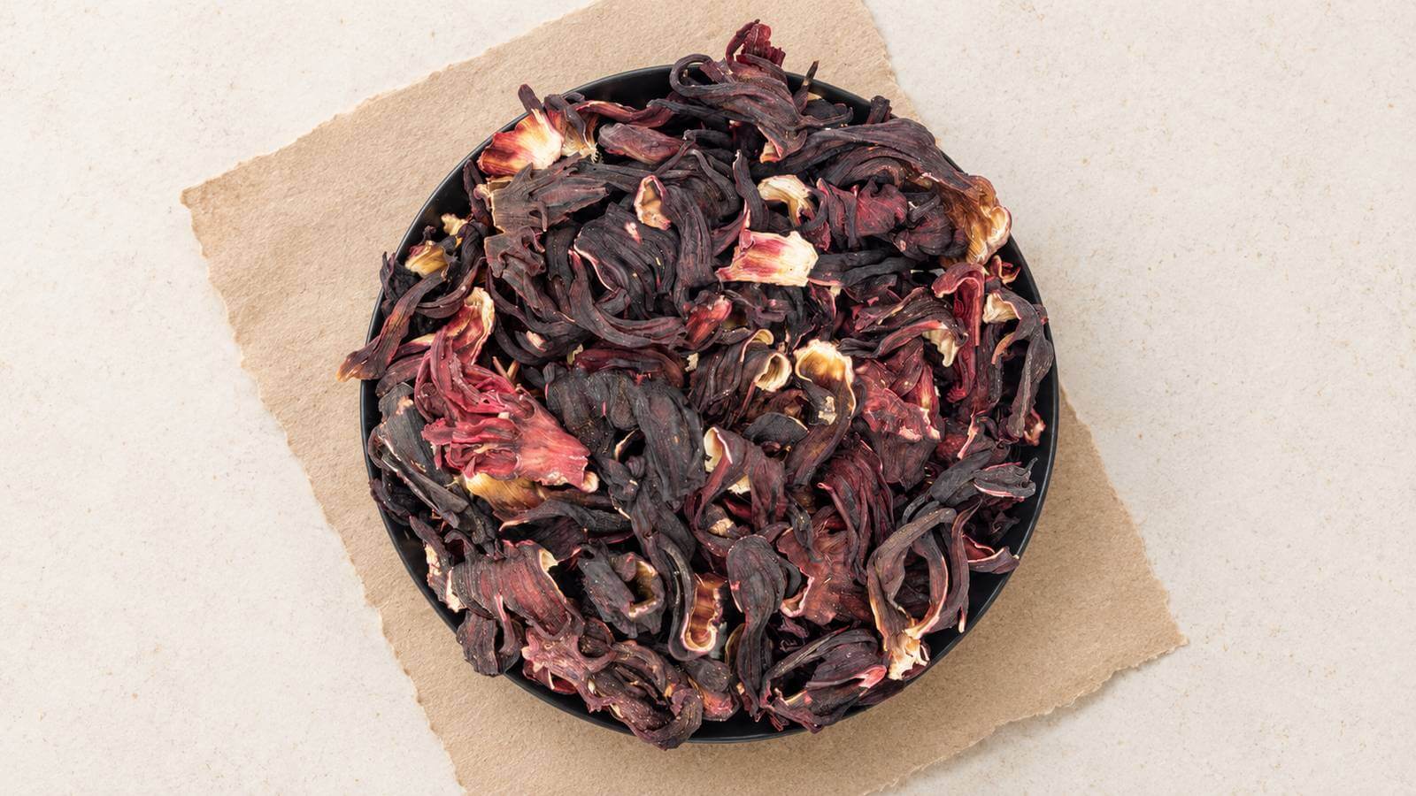 Mörkt vinröda torkade hibiskuskalkar med veckade ytor och ljusa snittytor i en mörk skål