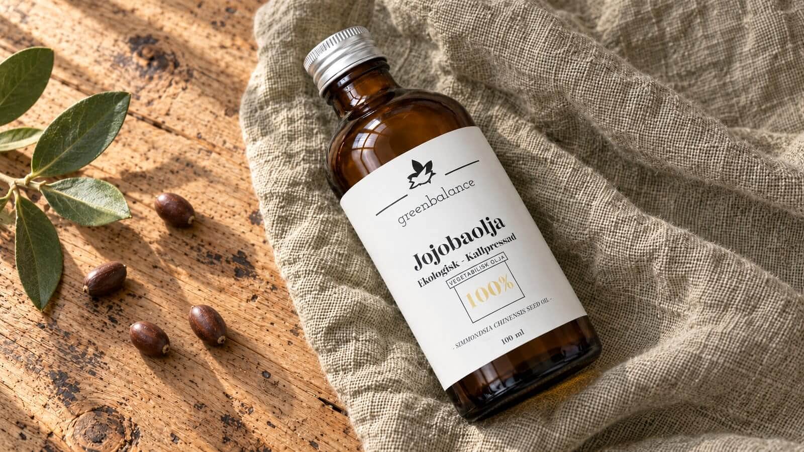 jojobaolja produkt ravaror Flaska med jojobaolja liggande på linne och trä, med jojobafrön och en kvist.