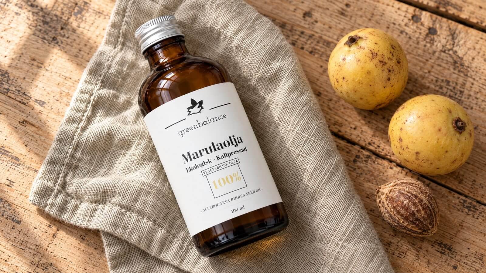 marulaolja produkt ravaror Flaska med marulaolja liggande på linne och trä, med gula marulafrukter och en kärna.