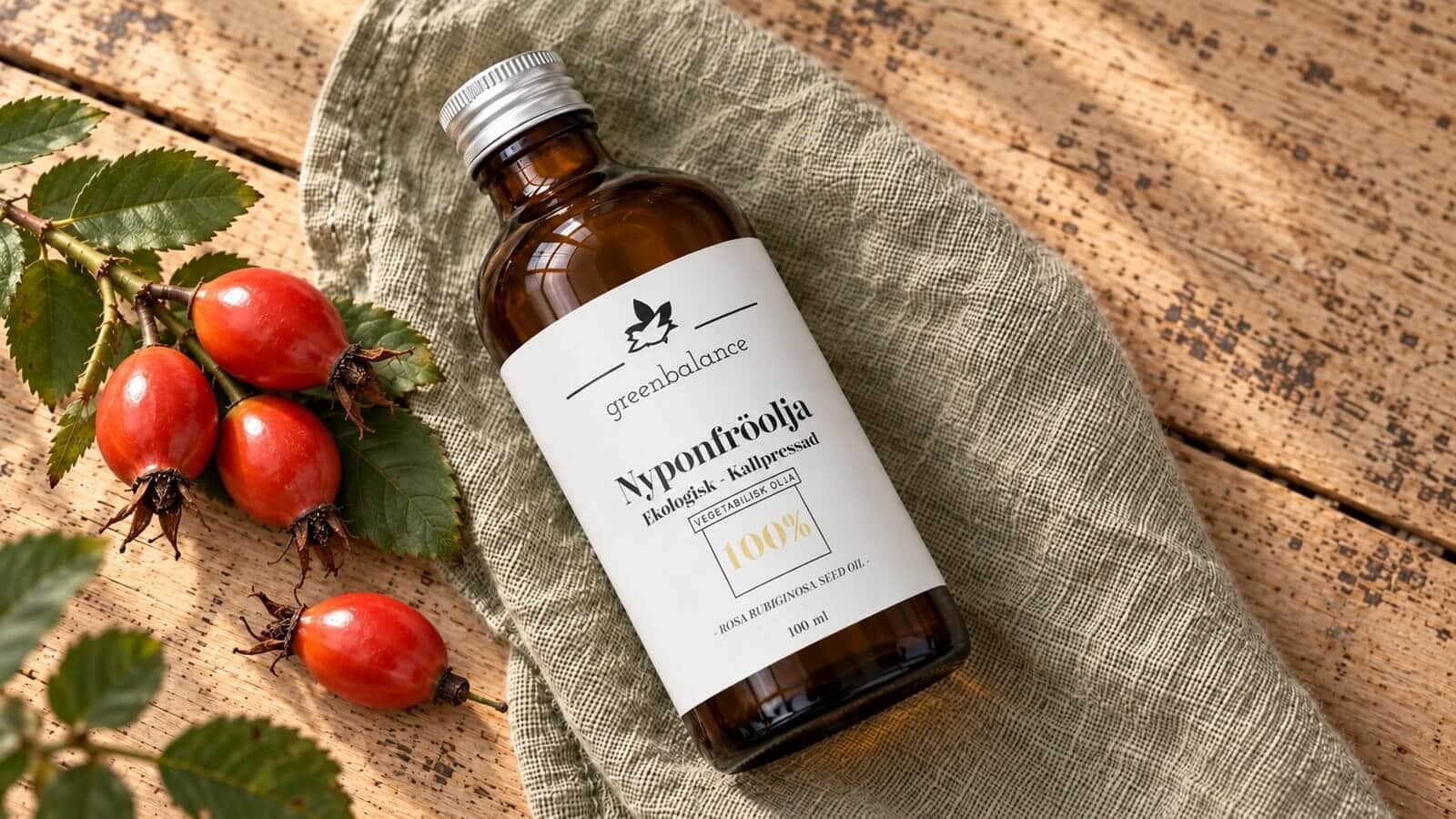nyponfroolja produkt ravaror Flaska med nyponfröolja liggande på linne och trä, med röda nypon och blad.