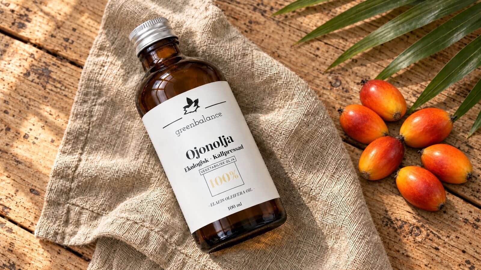 ojonolja produkt ravaror Flaska med ojonolja på linne och trä, med orange palmfrukter och ett grönt palmblad.