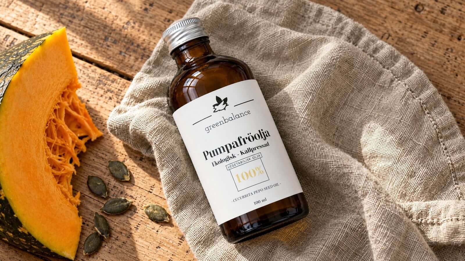 pumpafroolja produkt ravaror Flaska med pumpafröolja liggande på linne och trä, med pumpaklyfta och pumpakärnor.