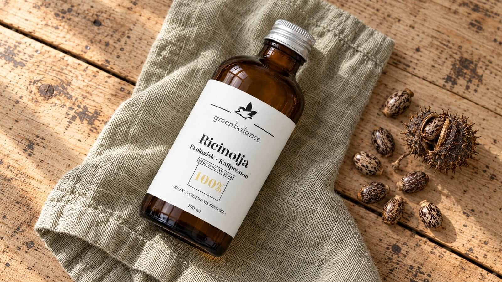 ricinolja produkt ravaror Flaska med ricinolja liggande på linne och trä, med ricinfrön och frökapsel.