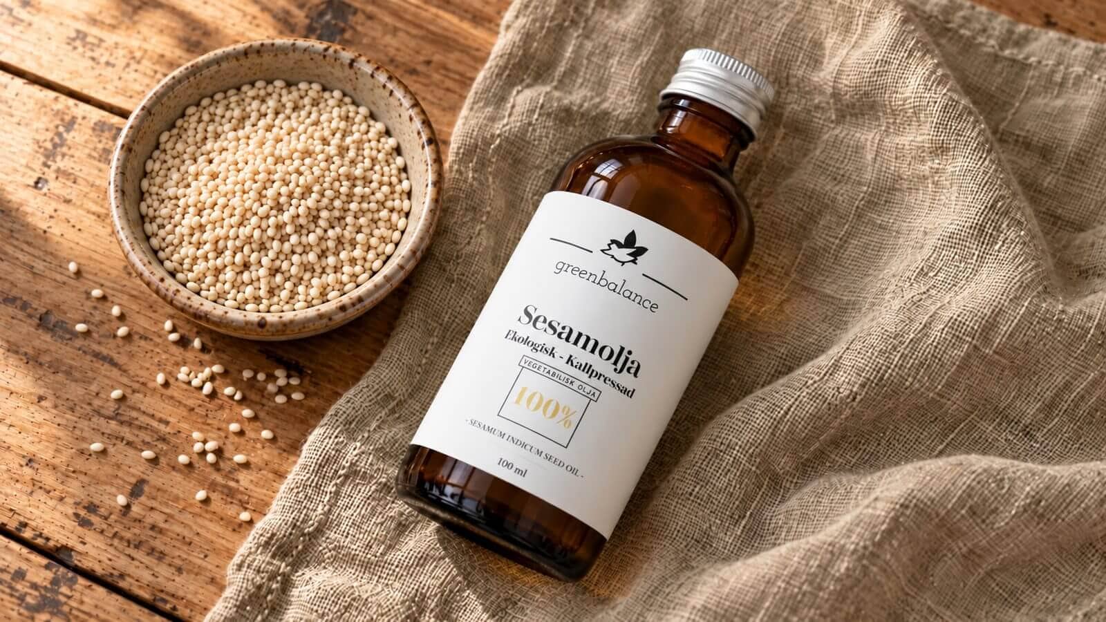 sesamolja produkt ravaror Flaska med sesamolja på linne och trä intill en bred keramikskål med ljusa sesamfrön.