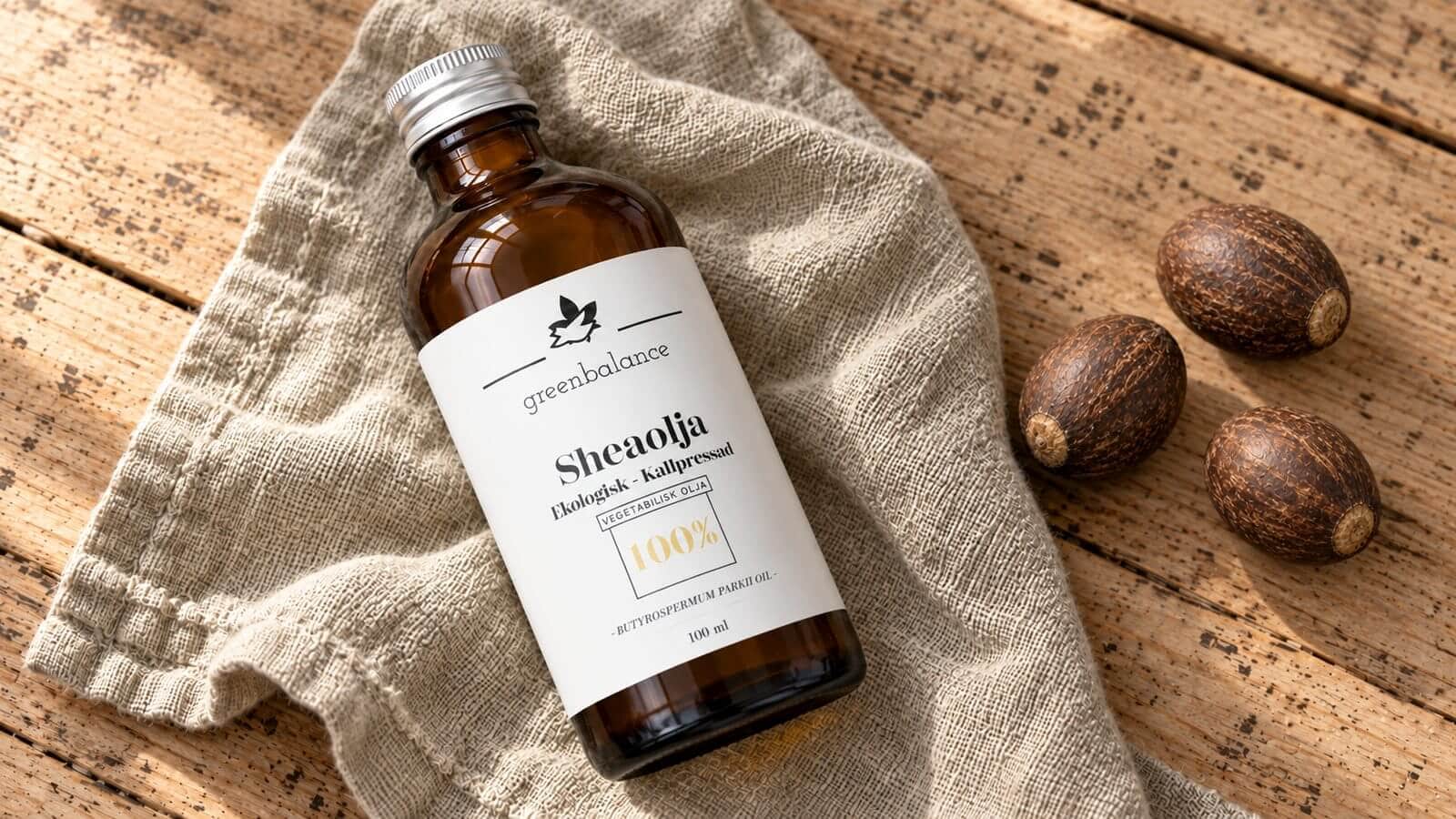 sheaolja produkt ravaror Flaska med sheaolja liggande på linne och trä, med hela sheanötter.